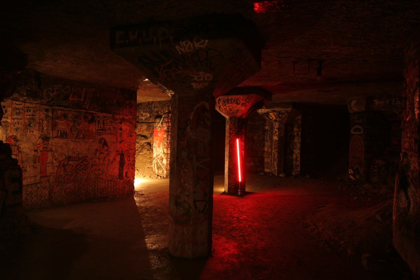 a study shot with a red-shining sara and a strong candle-like source drawing light on walls and columns in an underground location