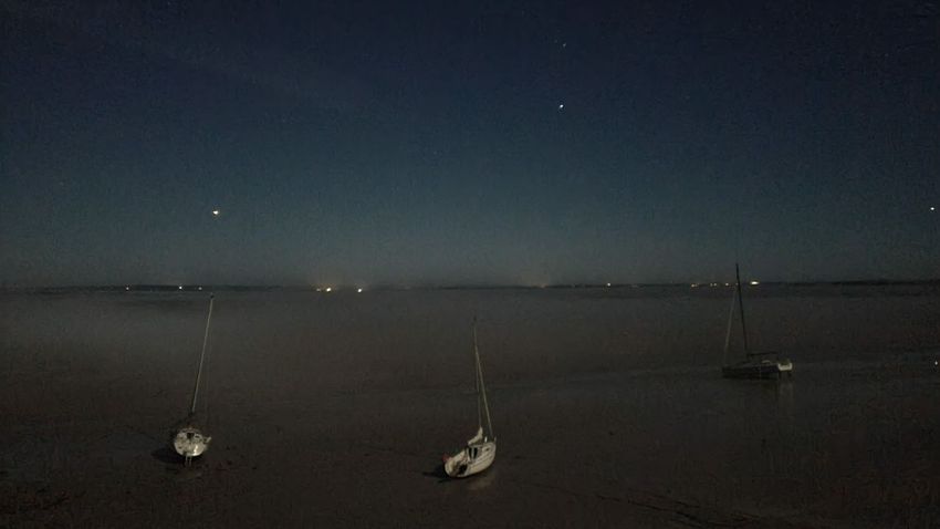 sous un ciel nocturne, trois petits voiliers de plaisance reposent sur le sable d'une grande baie